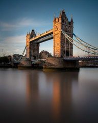 Fototapeta na wymiar Tower Bridge located in London city, United Kingdom with beautiful blue sky background. Calm River Thames in long exposure shot with tourism, tourist view in city landscape