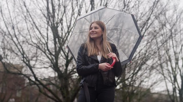 A beautiful young woman twirls an umbrella and similes on a rainy day in the city