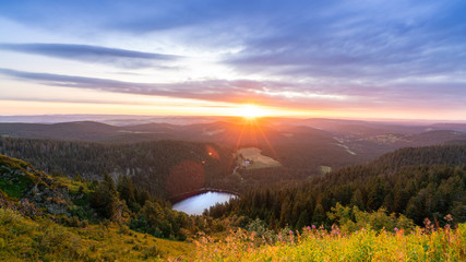 Beatiful mountains and lake at sunrise, green forest under golden sunlight and clouds in the sky