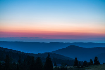 Sunrise over mountains, blue sky, and orange cloulds on the horizon; natrual landscape in the morning