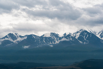 Fototapeta na wymiar snowy mountain peaks on horizon of valley under clouds, travel to mountain area
