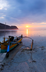 An Indonesian fishing canoe or Jukung rest on a beach of the island of Sumbawa in Indonesia during the low tide at sunset time