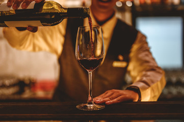 The bartender is pouring red wine in glasses and many empty glasses on the bar counter. Blurred background. wine , cocktail, alcohol, beverage, restaurant, relax concept.