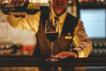 The bartender is pouring red wine in glasses and many empty glasses on the bar counter. Blurred background. wine , cocktail, alcohol, beverage, restaurant, relax concept.