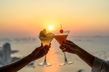 Couple enjoying of Cheers glass of cocktail in a restaurant  at sunset view sea. Cocktail, Couple, Honeymoon, Dinner, Wine, Romantic concept.