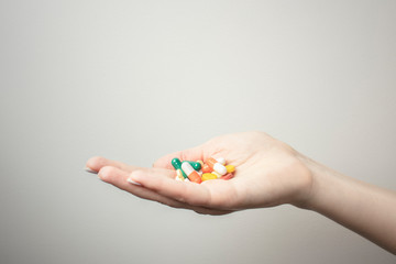 A handful of various pills in a woman's hands. Medications against the COVID-19 and other conditions and diseases on the grey background. Medicine.