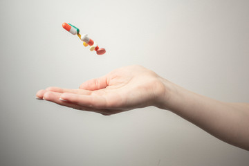 A lot of different pills falling into woman's hands. Drugs against the COVID-19 and other conditions and diseases on the white background.