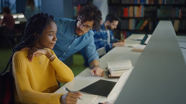 University Library: Gifted Black Girl uses Laptop, Smart Classmate Explains and Helps Her with Class Assignment. Happy Diverse Students Talking, Learning, Studying Together for Exams