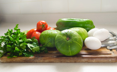 Wooden table with some vegetables, zucchinis, tomatoes, parsley, green pepper  and eggs.