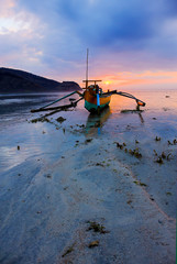 An Indonesian fishing canoe or Jukung rest on a beach of the island of Sumbawa in Indonesia during the low tide at sunset time