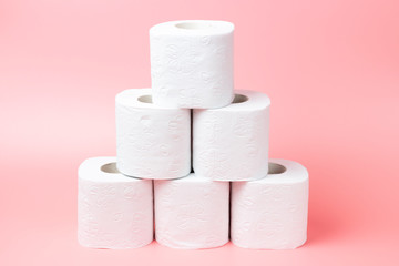 A stack of white rolls in toilet paper on a pink background close up.