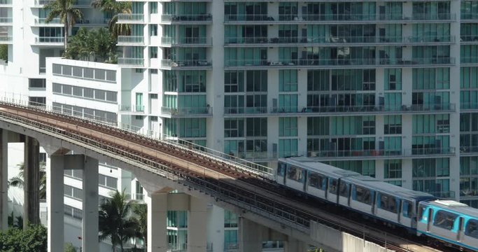 Train passing by over a small bridge in the middle of the city next to large flat.