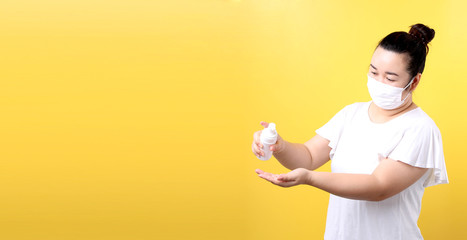 Asian woman using alcohol gel and wearing medical mask,Recommend the prevention of viruses and various diseases. isolated on yellow background in studio With copy space.