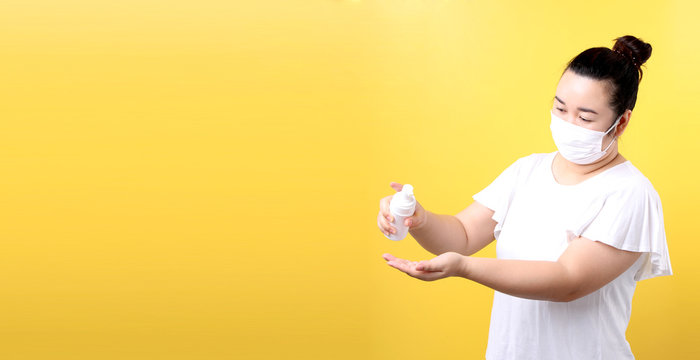 Asian woman using alcohol gel and wearing medical mask,Recommend the prevention of viruses and various diseases. isolated on yellow background in studio With copy space.