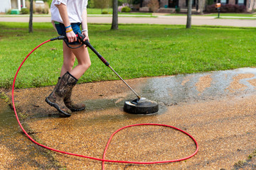 Woman pressure washing to clean driveway of a home