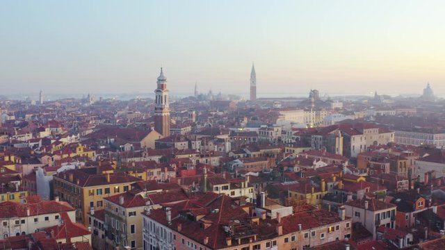 Aerial, tracking, drone shot overlooking building, streets and a church, at sunset, in Venice city, Italy