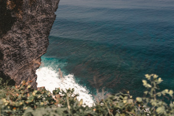 Beautiful girl with long hair on a huge rock overlooking the ocean. Cliff with the waves of the Indian Ocean in Bali. Indonesia. Travels