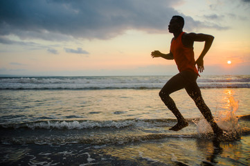 silhouette of young athletic and fit african american sport man doing running workout on sunset at the beach training hard jogging barefoot in healthy lifestyle concept