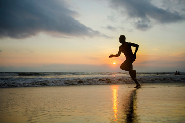 Fototapeta na wymiar silhouette of young athletic and fit african american sport man doing running workout on sunset at the beach training hard jogging barefoot in healthy lifestyle concept