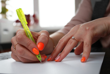 female hands with bright manicure write on paper
