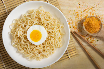Boiled egg with instant noodles on a white plate, placed on a wooden table.