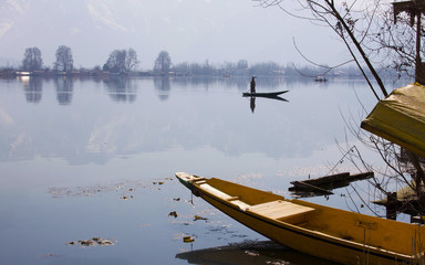 Small boat on the shore of Dal Lake in Srinagar, capital of Kashmir. Man on paddleboat in background.