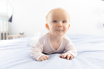 Cheerful adorable red haired baby girl crawling on bedding. Six month child lying on belly in bedroom. Childhood or baby care concept