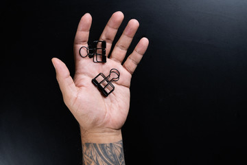 A man hand holdind black paper clips isolated on Black background.