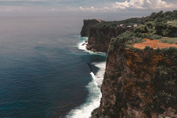 Fototapeta na wymiar Beautiful girl traveler with long hair and a slender body stands on a cliff of a cliff overlooking the waves of the blue ocean.Bali Island, Indonesia. Travel and tourism concept in exotic and tropical