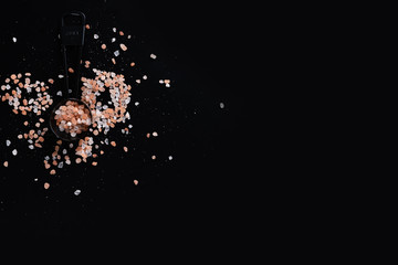 Black measuring spoons with Himalayan salt on black background.