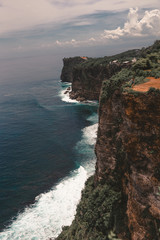 Fototapeta na wymiar Beautiful girl traveler with long hair and a slender body stands on a cliff of a cliff overlooking the waves of the blue ocean.Bali Island, Indonesia. Travel and tourism concept in exotic and tropical