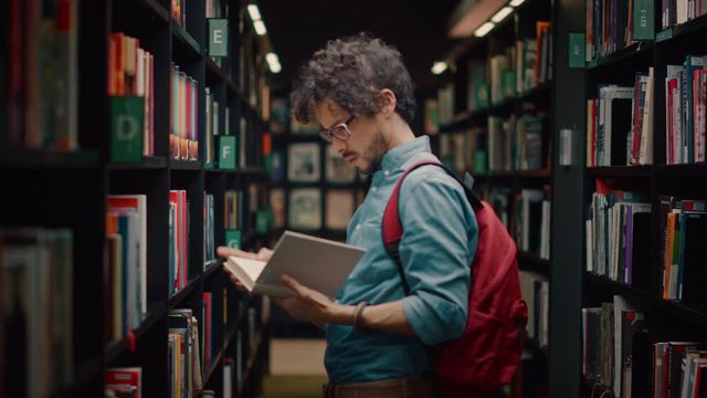 University Library: Portrait of Smart Hispanic Boy Walking Between Rows of Bookshelves Searching for the Right Book Title for Class Assignment. Focused Student Learning, Studying for Exams