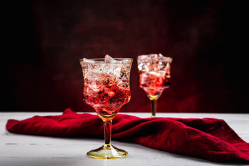 Two beautiful refreshing sparkling cocktails with ice, white wooden table, dark background with red tint, red napkin