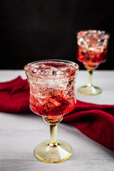 Two beautiful refreshing sparkling cocktails with ice, white wooden table, dark background, red napkin