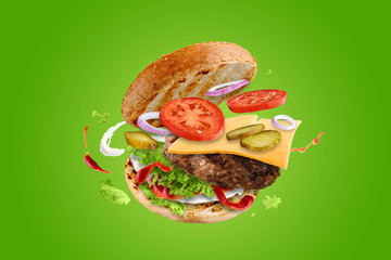 Big tasty hamburger with flying elements. Flying burger. Green background.