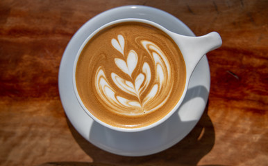 Close up of coffee cup with coffee latte art on a top. Latte art coffee over wooden background.