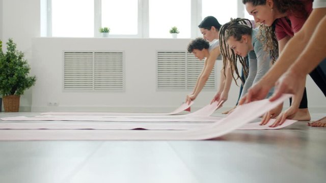 Low shot of yoga class students unrolling mats on laminate floor in light studio ready for sports exercises. Active lifestyle and young people concept.