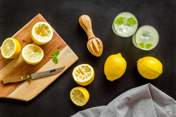 Homemade lemonade in glasses near juicer and cut lemons on black background top-down