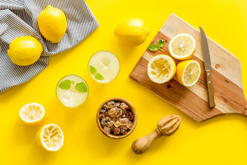 Homemade lemonade in glasses near juicer and cut lemons on yellow background top-down