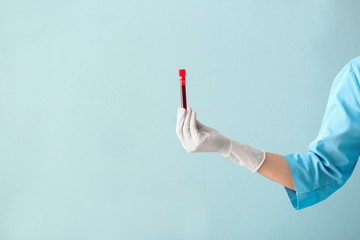 Doctor's hand holding test tube with blood sample on color background - Powered by Adobe