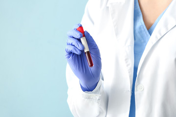Doctor holding test tube with blood sample on color background, closeup
