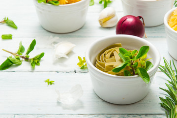 uncooked pasta variations and fresh spices on white wooden table