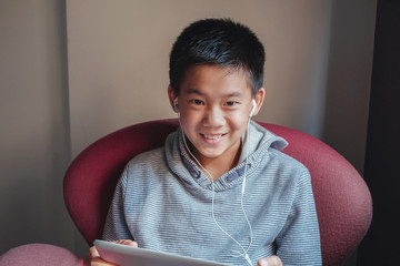oung  mixed Asian preteen boy using digital tablet at home, listening to podcast, gaming, online...