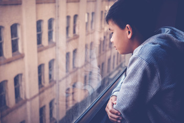 Sad Asian preteen boy feeling lonely, looking out of window from his room, social distancing,...