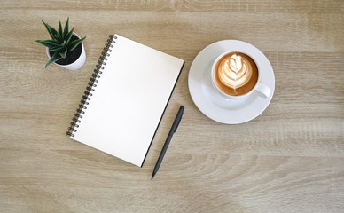 top view of notebook next to a pen and cup of coffee on wooden table with copy space.