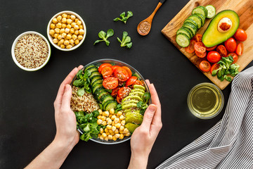 Quinoa, avocado and chickpeas in bowl in hands - balanced healthy food - on black table. Top view