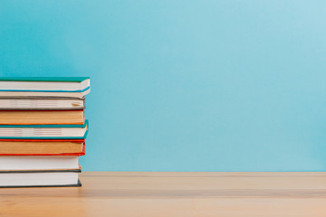 A simple composition of many hardback books, raw books on a wooden table and a bright blue background. Going back to school. Copy space. Education.