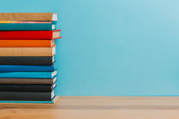 A simple composition of many hardback books, raw books on a wooden table and a bright blue background. Going back to school. Copy space. Education.