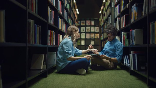 University Library Study: Smart Caucasian Girl Sitting and Talented Hispanic Boy Sitting Cross-Legged On the Floor, Talk, Use Laptops, Collaborate and Discuss Paper, Study and Prepare for Exams