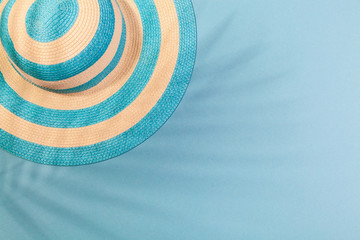 Top view on beach accessories on turquoise blue background - striped blue hat in the shadow of palm leaf. Concept of beach holiday, sea tour, warm sunny summer. Advertising space